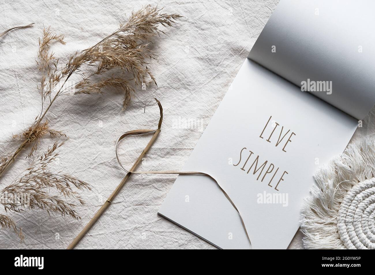 Testo Live semplice nella nota a blocchi. Busta, macramè e pampas erba.. Semplice piatto minimo posato su tessuto avorio con canne colorate in terra asciutta. Naturale Foto Stock