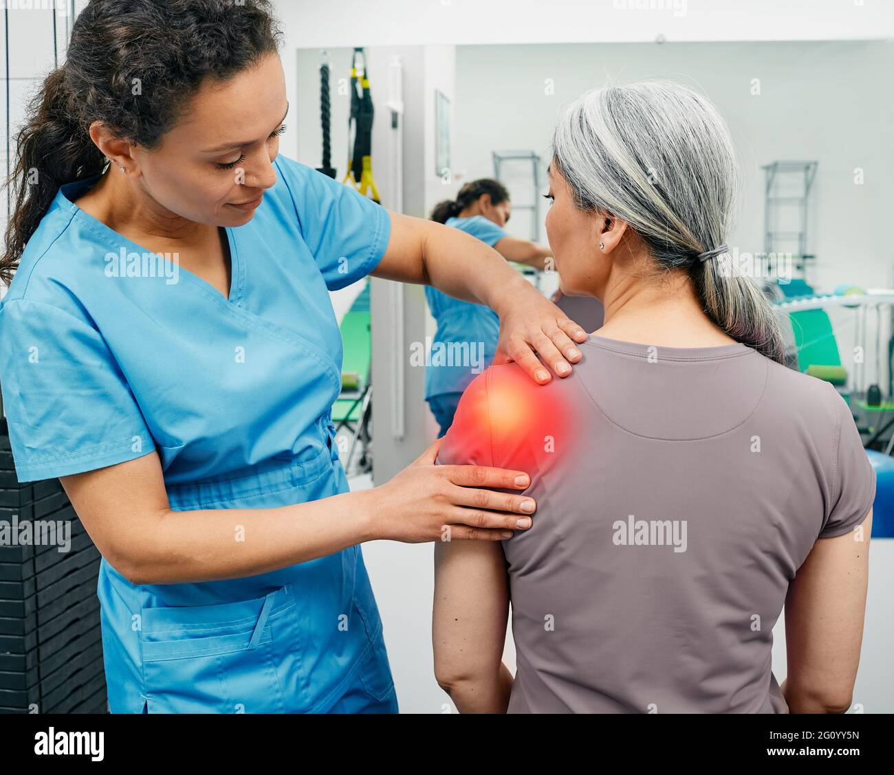 Fisioterapista esamina una paziente con dolore alle articolazioni delle spalle in una clinica di riabilitazione. Donna con una ferita della spalla visita il suo chiropractor Foto Stock