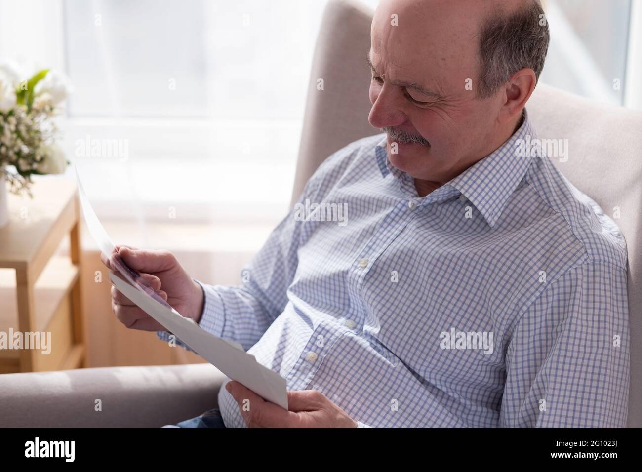 Uomo anziano da solo seduto sul divano a casa tenendo foto pensando ai ricordi Foto Stock
