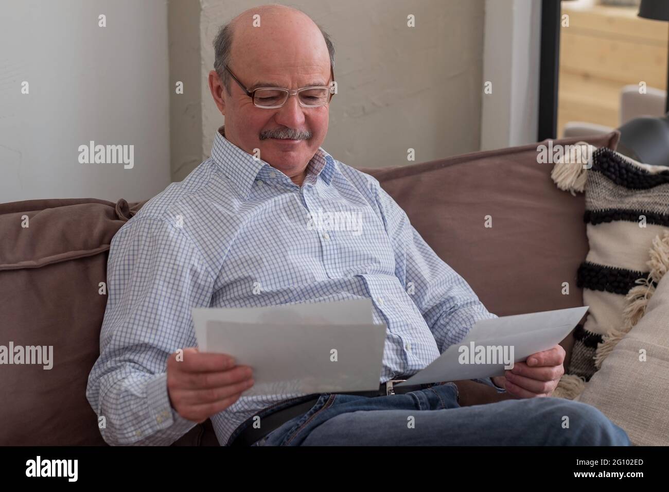 Uomo anziano da solo seduto sul divano a casa tenendo foto pensando ai ricordi Foto Stock