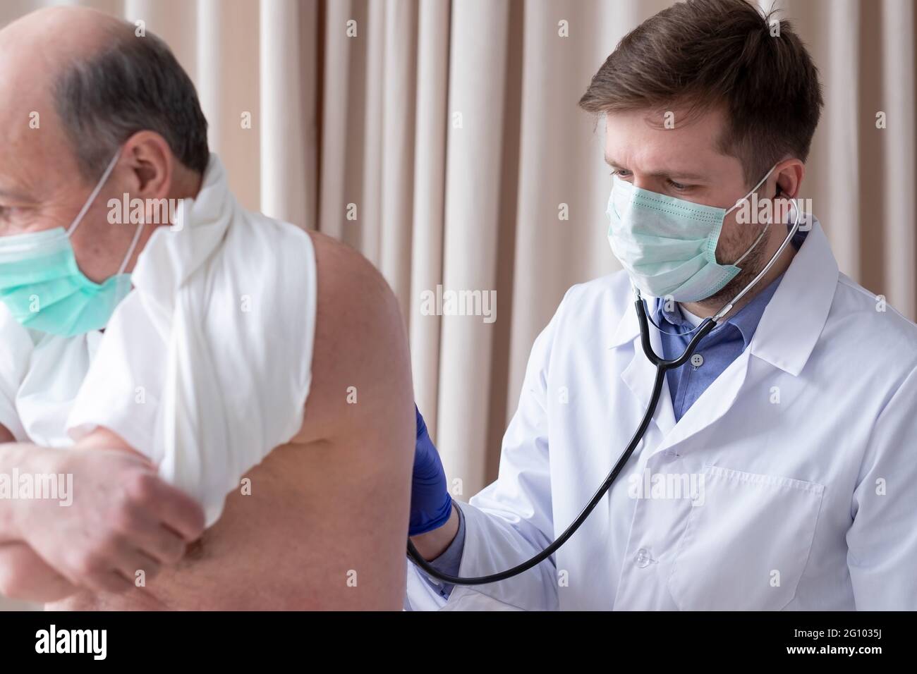 Il medico maschio di Caucaian ascolta la respirazione di un maschio anziano con uno stetoscopio Foto Stock