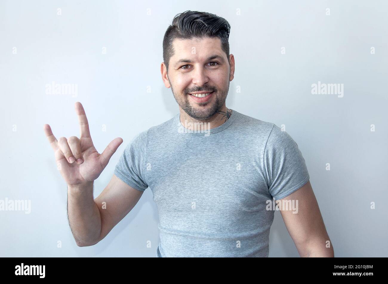 Ritratto di un giovane felice che si diverte e mostra corni gesto della mano. Raffigurante un segno di roccia di metallo pesante. Foto Stock