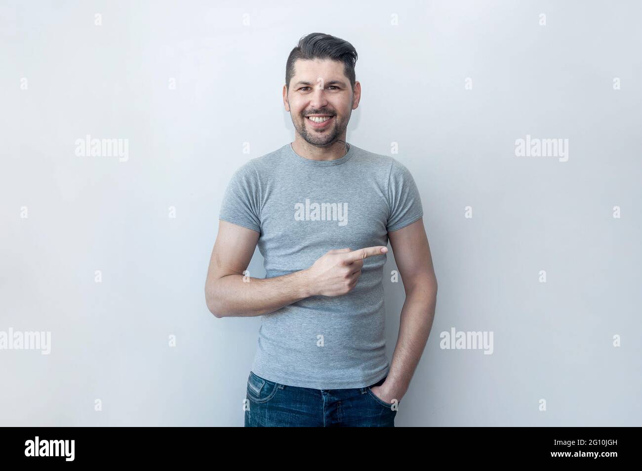 Bell'hipster sorridente uomo che punta via con stupore mentre mostra nuova offerta . Guarda là! Attenzione assente, punta con il pollice. Foto Stock