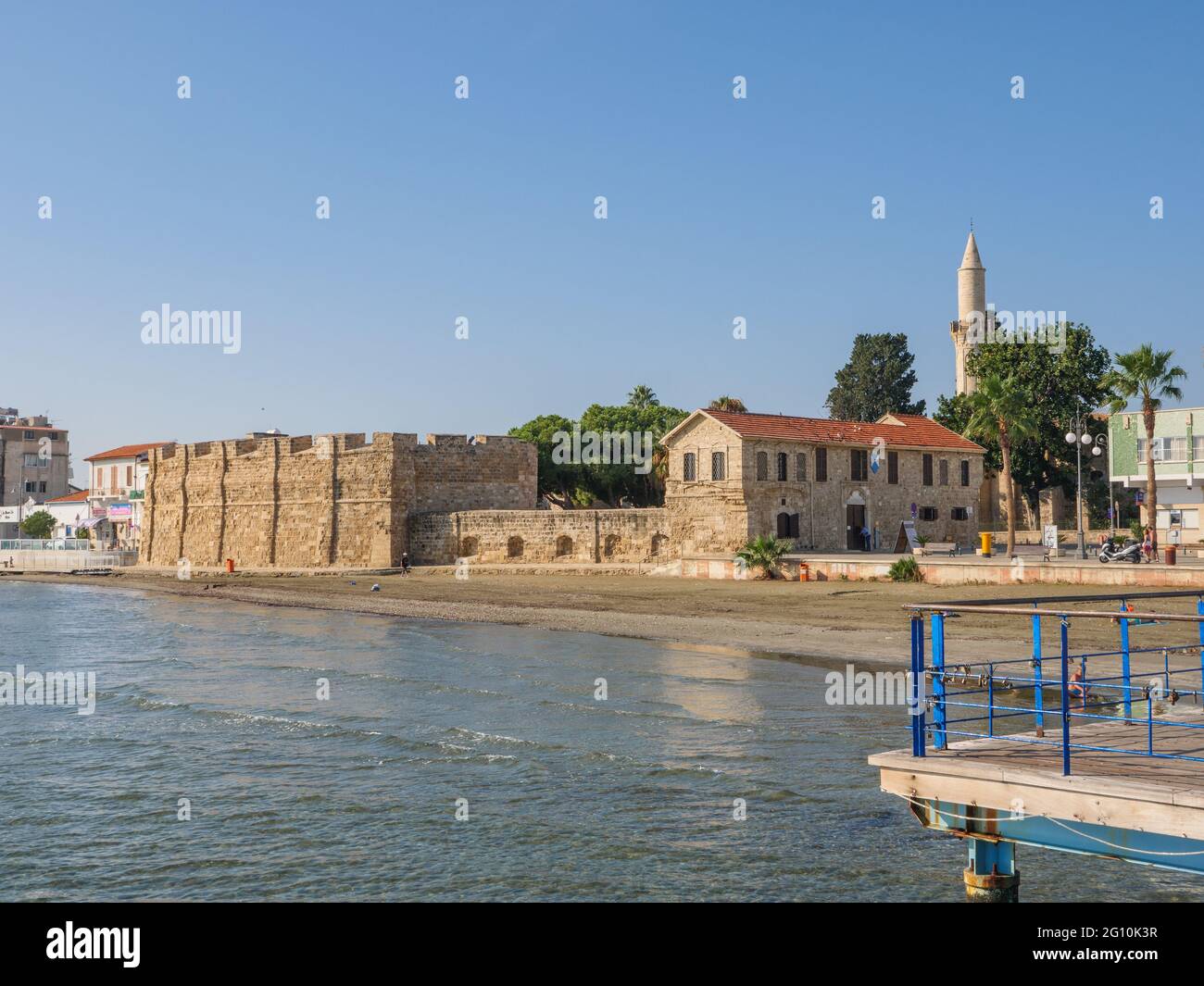Vista dal molo sull'antica fortezza di Larnaca, la torre della moschea di Djami Kebir e la spiaggia con sabbia vulcanica in una giornata di sole a Cipro. Foto Stock