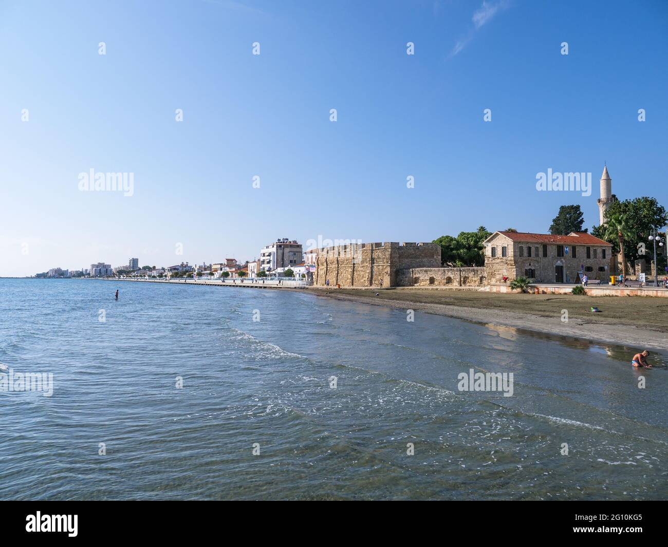 Vista dal molo sull'antica fortezza di Larnaca, la torre della moschea di Djami Kebir e la spiaggia con sabbia vulcanica in una giornata di sole a Cipro. Foto Stock