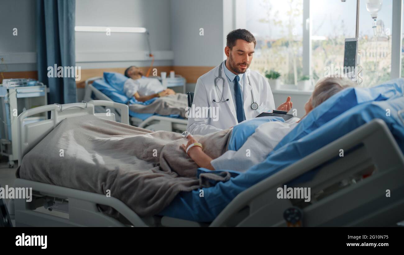 Hospital Ward: Friendly Doctor parla con bella paziente femminile anziano che riposa a letto, spiega risultati dei test, dà consigli di recupero. Il medico parla Foto Stock