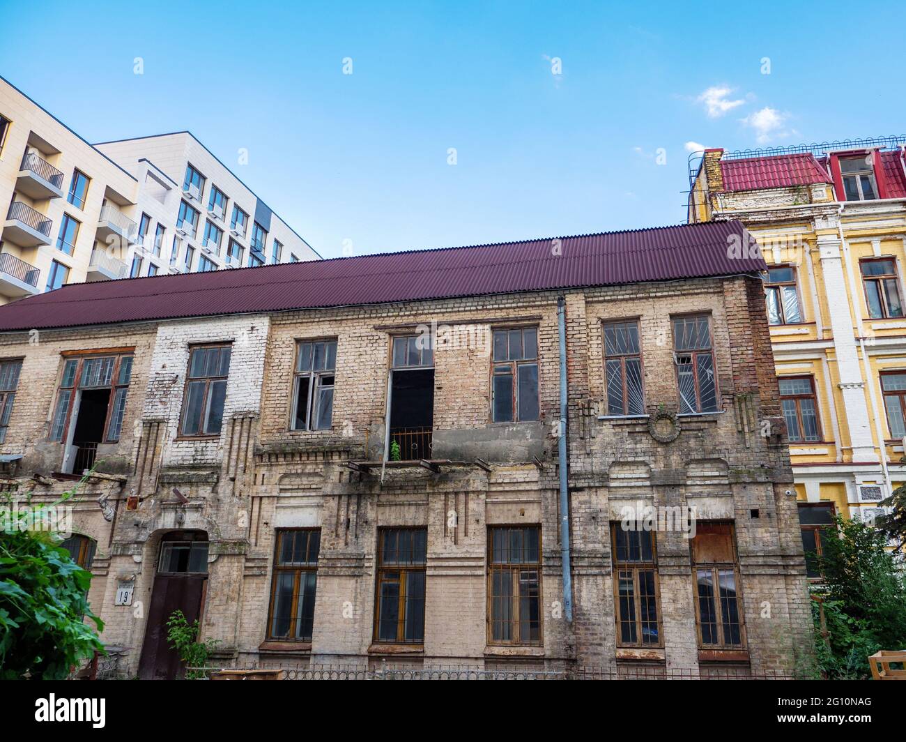 L'esterno di un vecchio edificio a due piani in mattoni forsaken e mezzo rovinato, all'ombra di un nuovo e alto edificio costruito di recente nel centro della città di Kiev, Ucraina. Foto Stock