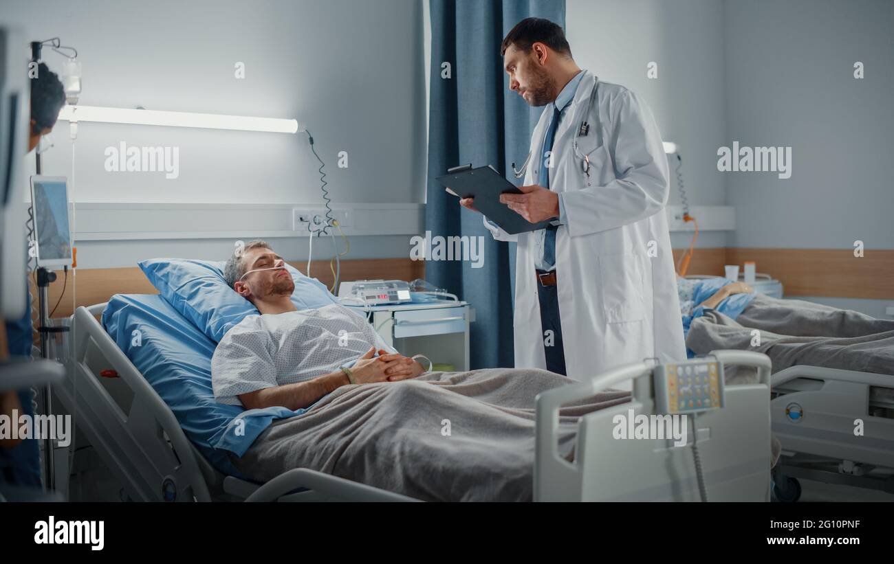 Hospital Ward: Medico amichevole fa il controllo sul bel paziente giovane maschio che dormiva in letto, controlla i suoi segni vitali, scrive le informazioni. Trattamento medico Foto Stock