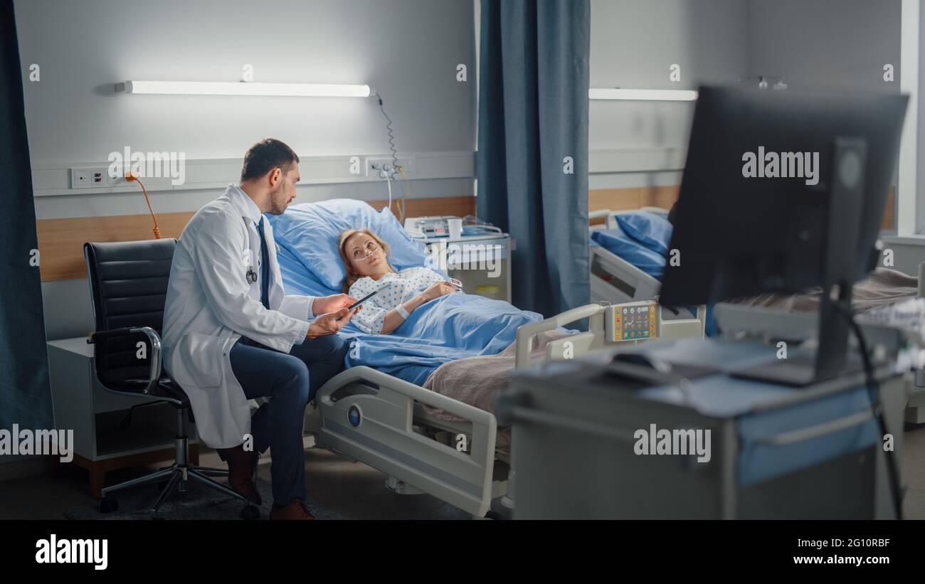 Hospital Ward: In Modern Equipment Clinic chirurgo utilizzando Tablet computer Consulenza paziente recupero dopo un intervento chirurgico di successo a letto. Moderno avanzato Foto Stock
