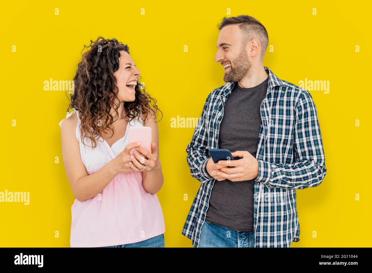 Felice coppia su sfondo di colore giallo ride con smartphone in mano Foto Stock