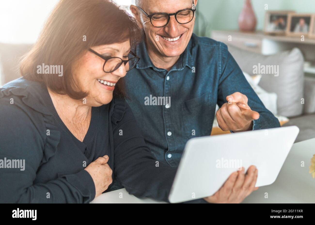 Coppia di mezza età sorridente mentre si acquista online - gli anziani chiacchierano con amici e familiari - filtro caldo sullo sfondo Foto Stock