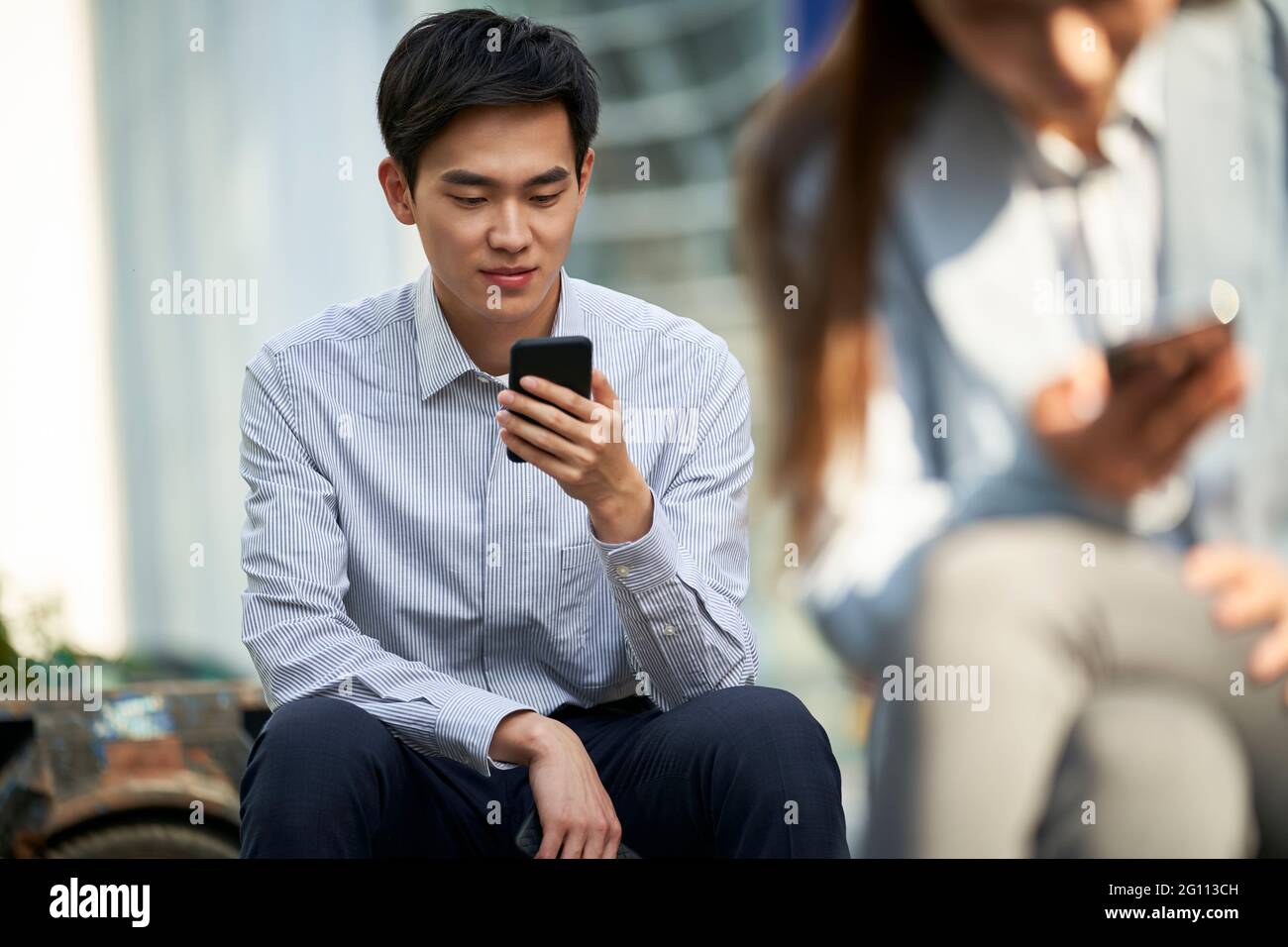 giovane lavoratore asiatico di ufficio che legge usando il cellulare all'aperto Foto Stock