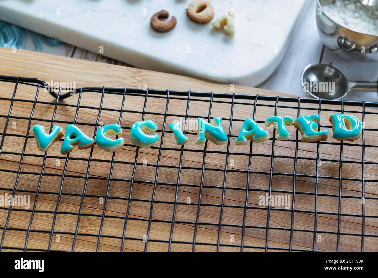 vaccinato scritto in biscotti che asciugano su una griglia di metallo su una tavola di legno con ghiaccio blu Foto Stock