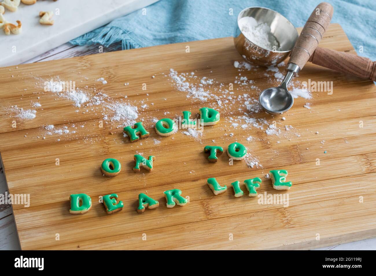Attenerci alla vita cara scritta con i biscotti su un tagliere di legno con cucchiai dosatori e farina su un tavolo con un panno blu Foto Stock