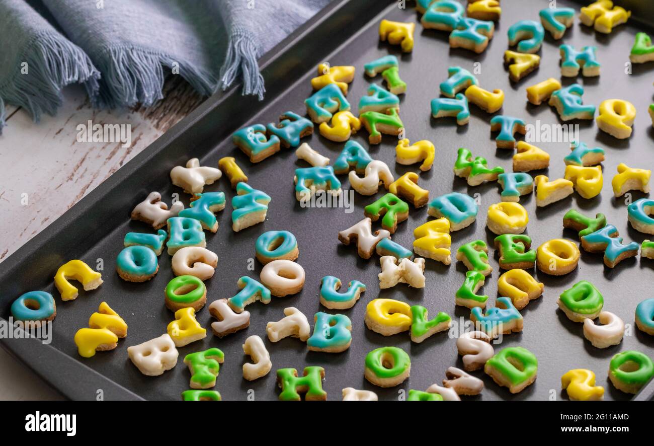 piatto da cucina scuro pieno di biscotti appena fatti con ghiaccio verde blu bianco e giallo su luce naturale Foto Stock