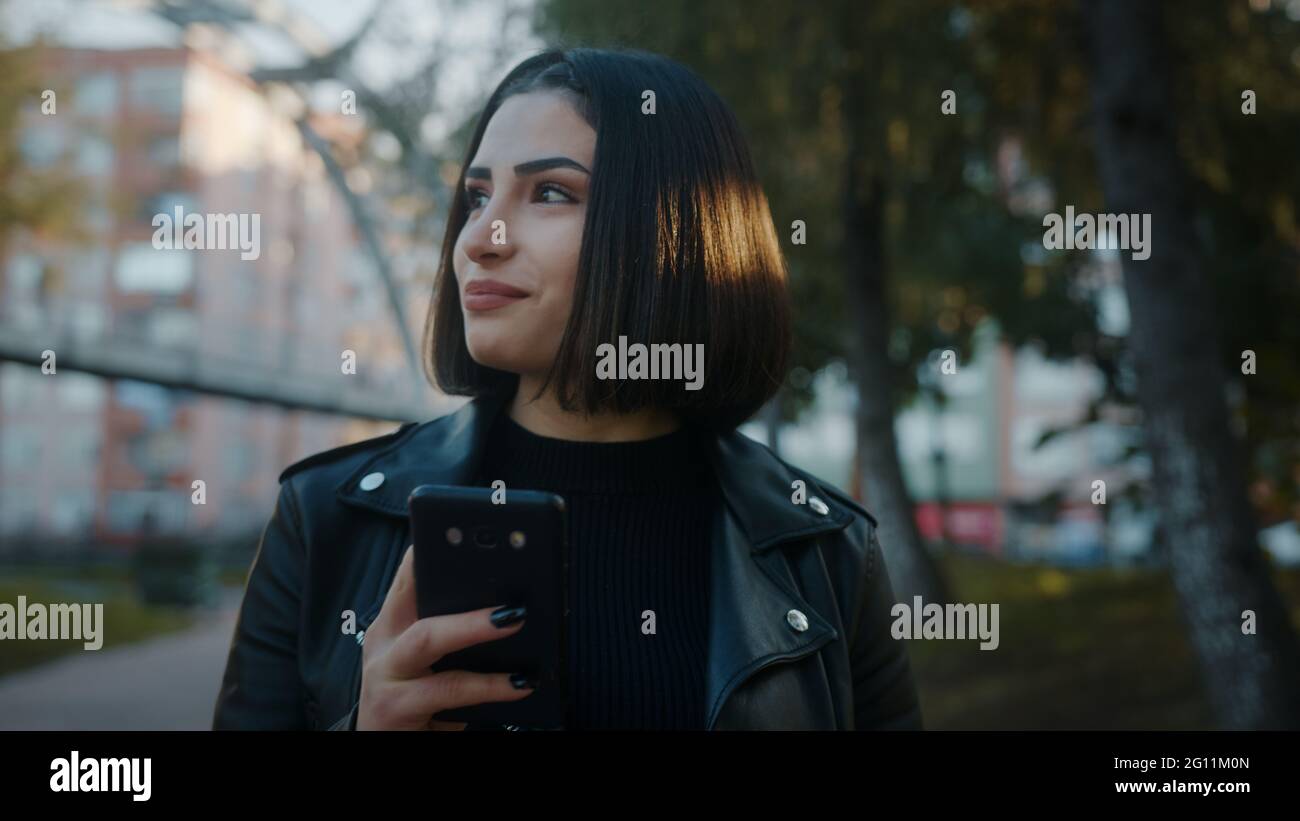 Giovane donna sorridente che cammina nel parco e usa lo smartphone. A piedi. Tempo libero nei social media di Internet. Chattare con gli amici, digitare un messaggio Foto Stock