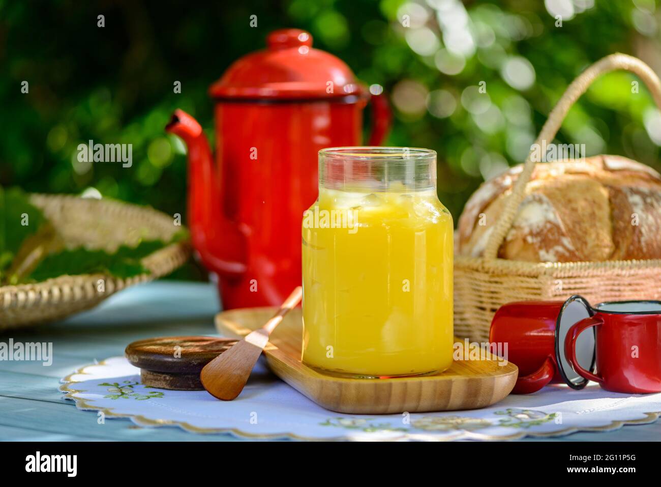 Burro di ghee in vaso di vetro sul tavolo della colazione con teiera e tazze rosse. Foto Stock