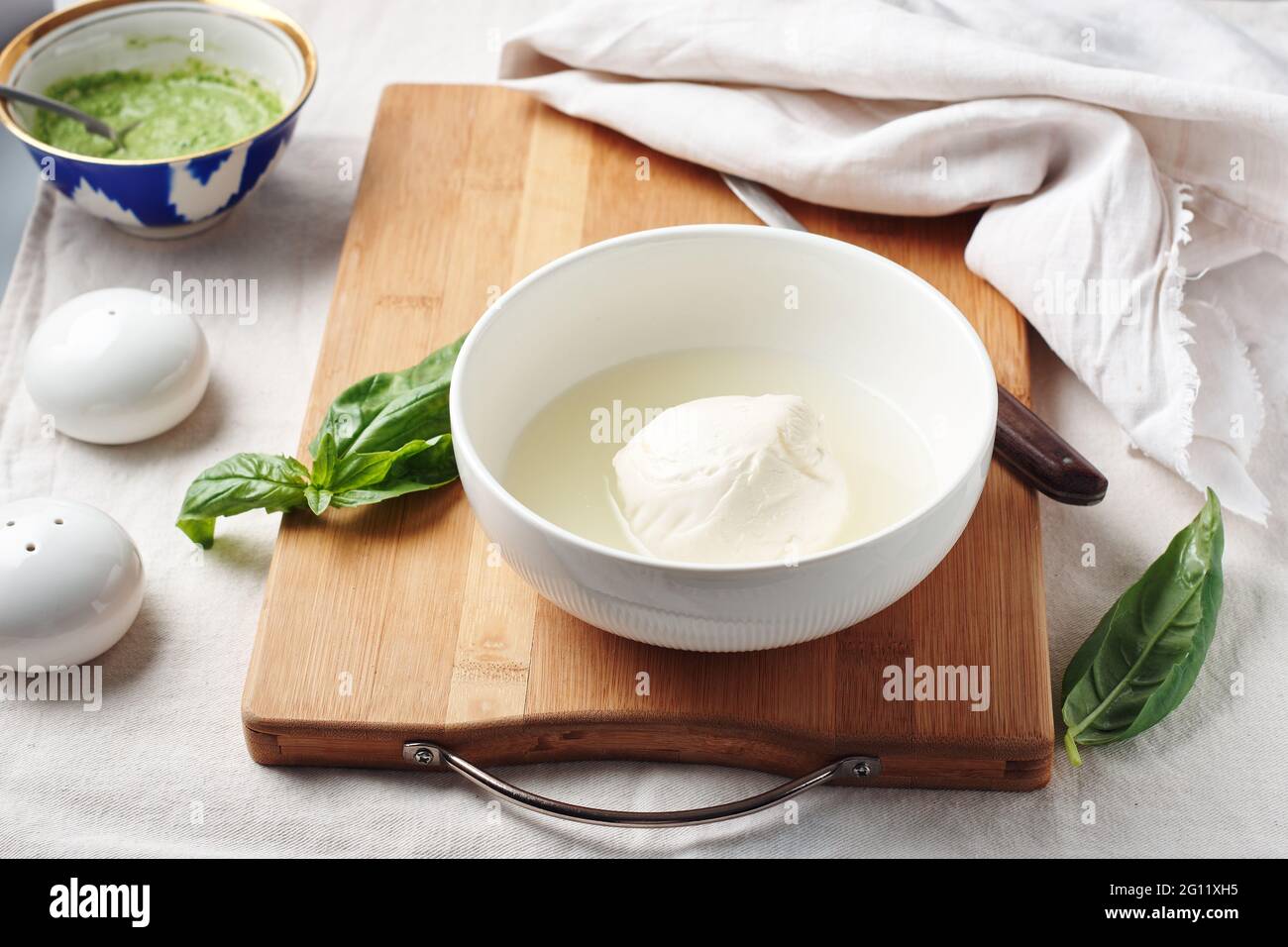 Palla di mozzarella in un recipiente e foglie di basilico fresco. Foto Stock