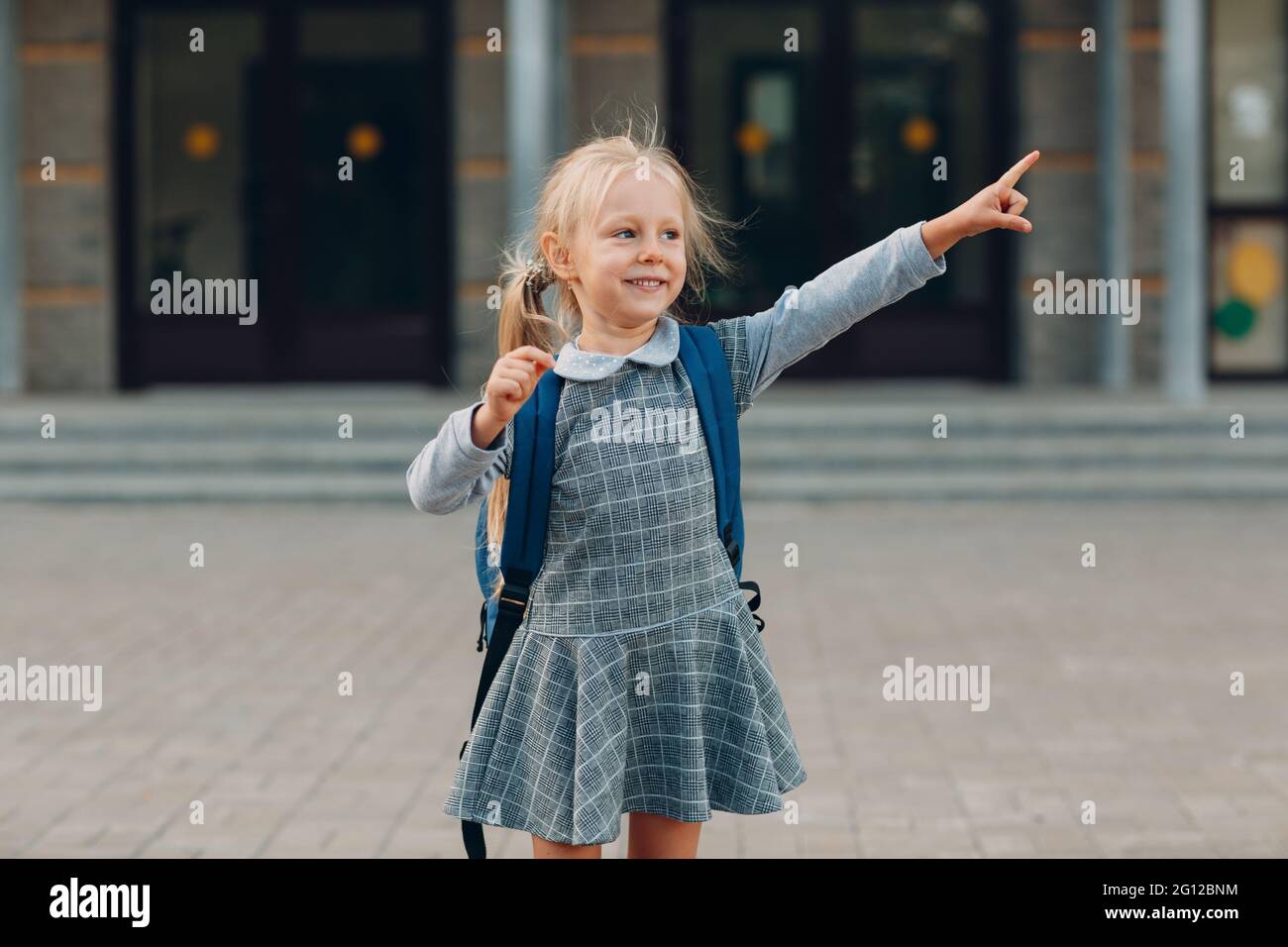 Carina bambina con zaino tornare a scuola e puntare il dito. Foto Stock