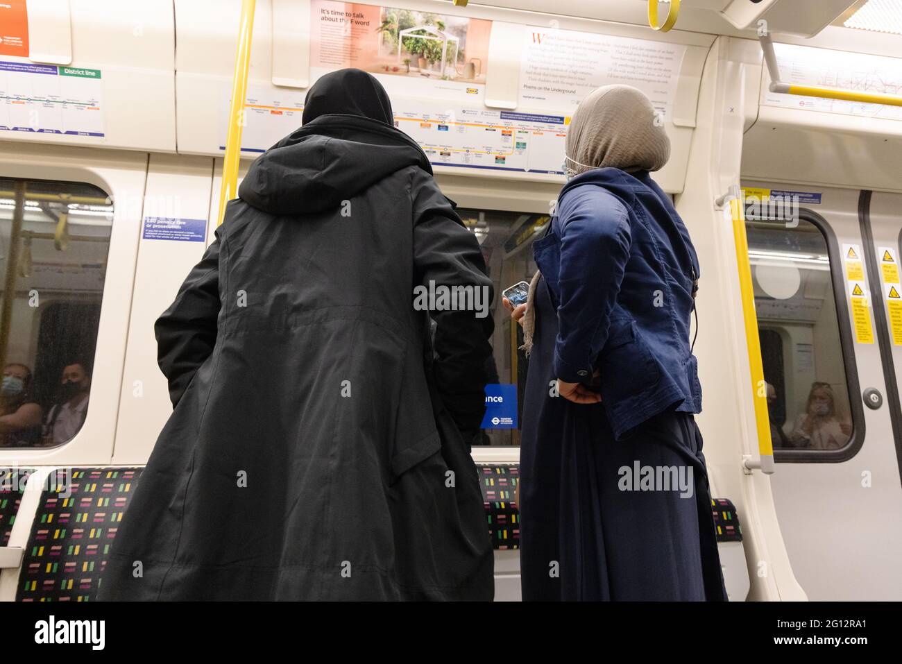Multiculturale Londra; Vista posteriore di due donne musulmane che viaggiano sulla metropolitana di Londra, in una carrozza, guardando la mappa della metropolitana, Londra UK Foto Stock