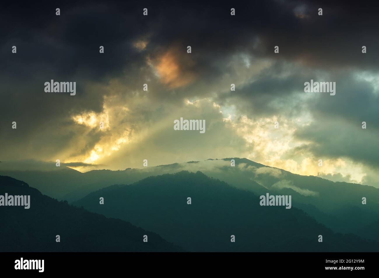 Luce proveniente da una finestra di nuvole dal sole che tramonta, sulle vette del Monte Himalayan. Suggestiva formazione di nuvole con colori del tramonto su mountta indiana Foto Stock