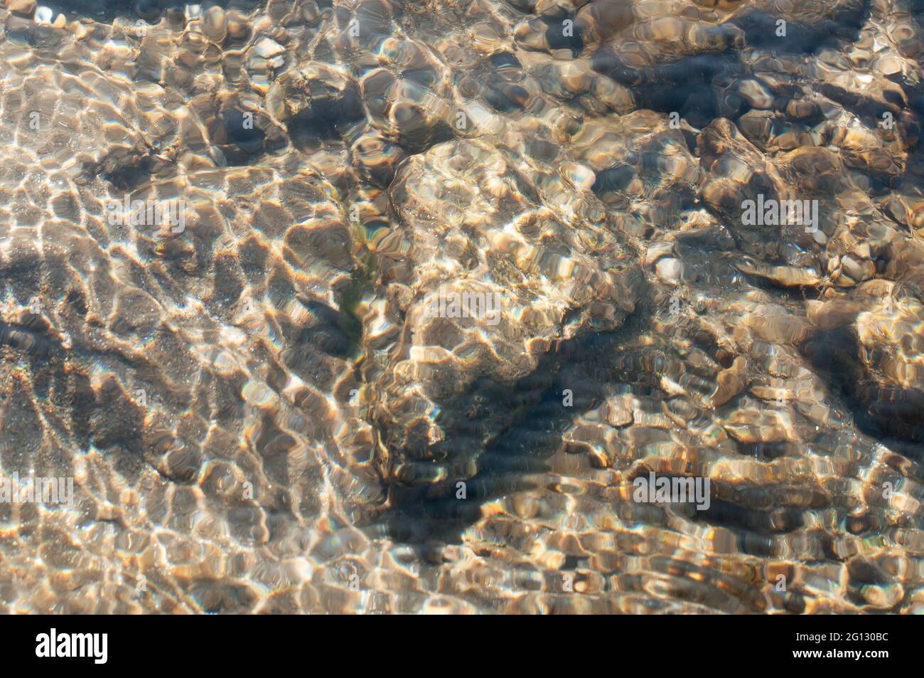 Raggi di sole che riflettono da pietre e rocce sott'acqua - creando un bel disegno astratto naturale. Immagine scattata al fiume Reshi, Sikkim, India Foto Stock