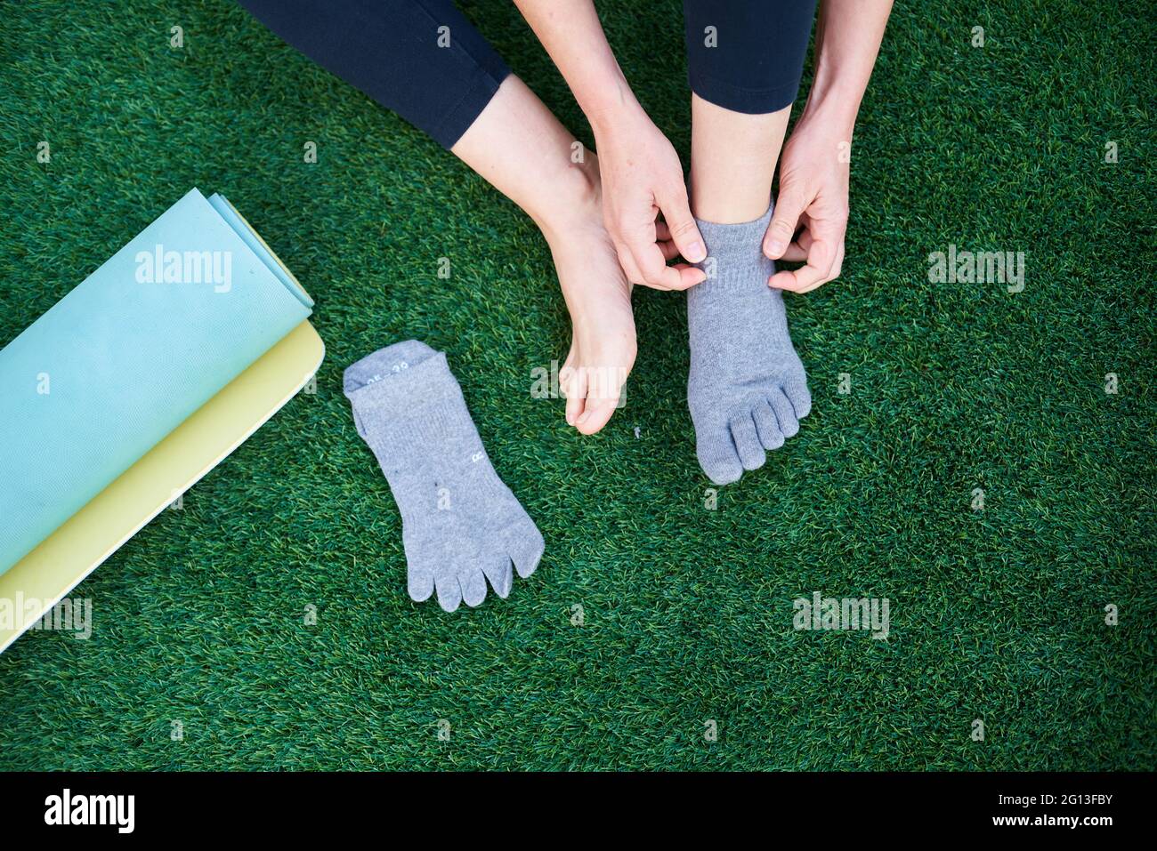 Primo piano delle mani di una donna che mette su calze yoga accanto a un tappetino in erba Foto Stock