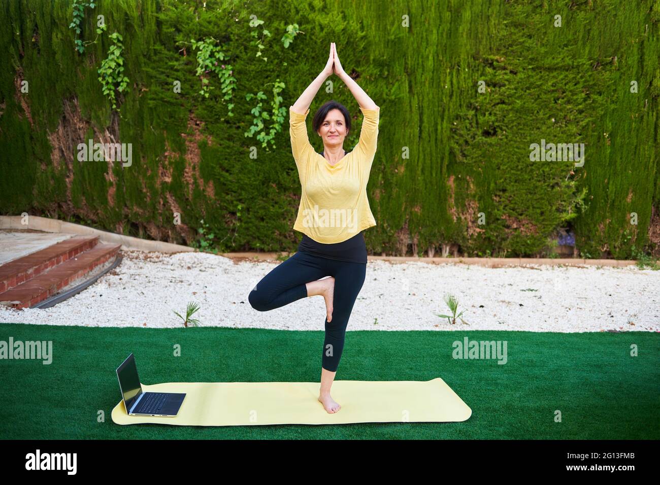 Una donna prende una lezione di yoga dal suo laptop all'aperto Foto Stock