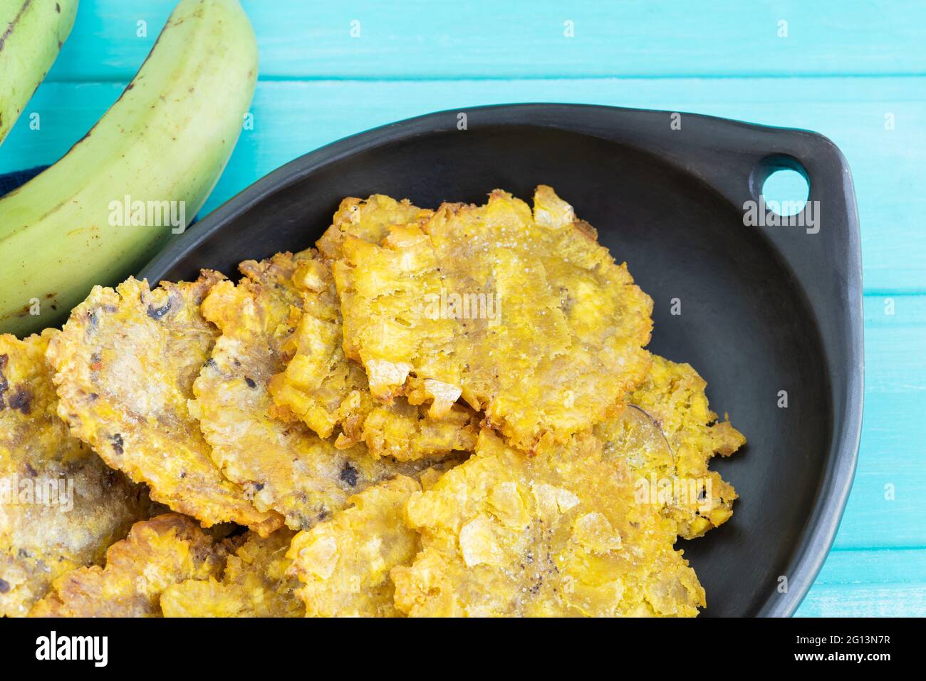 Pataconi fritti in piastra nera su sfondo di legno blu. Spazio di copia. Foto Stock