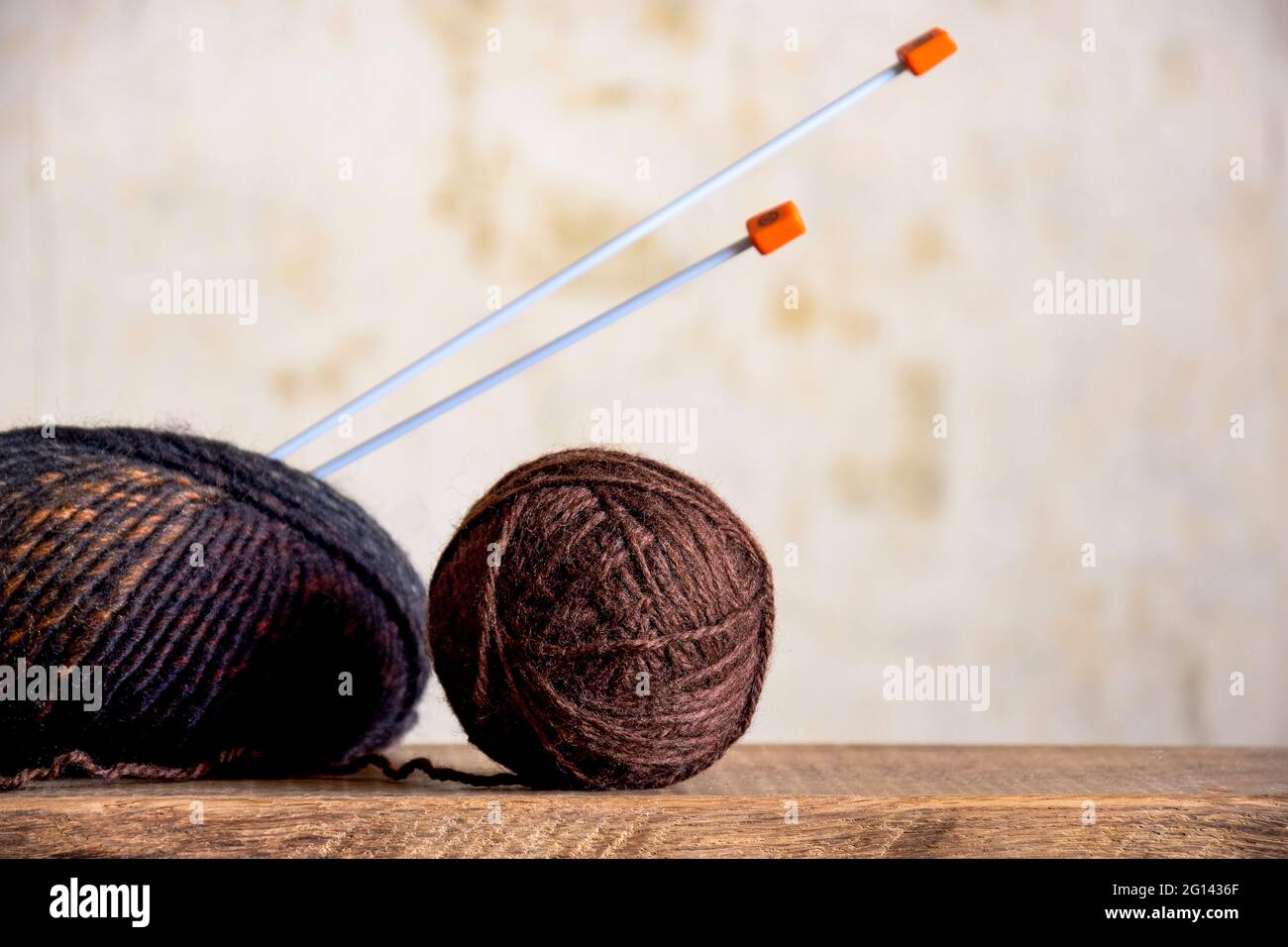 due matasse di filo di lana in tonalità marrone e aghi da maglieria su una vecchia superficie di legno primo piano, fatta a mano, maglia Foto Stock