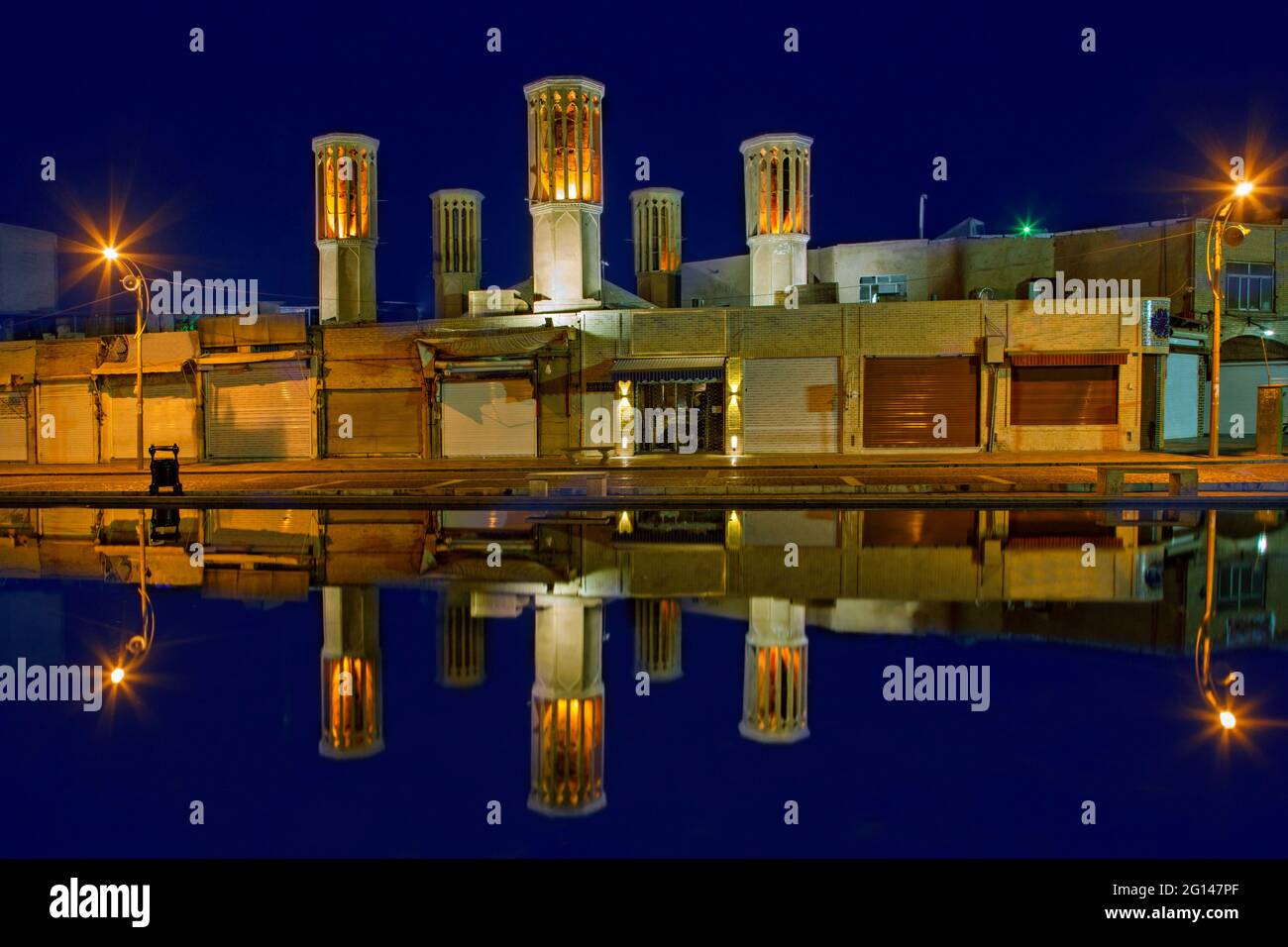 Torri eoliche e riflessi nello stagno, al crepuscolo, nell'antica città di Yazd, Iran Foto Stock