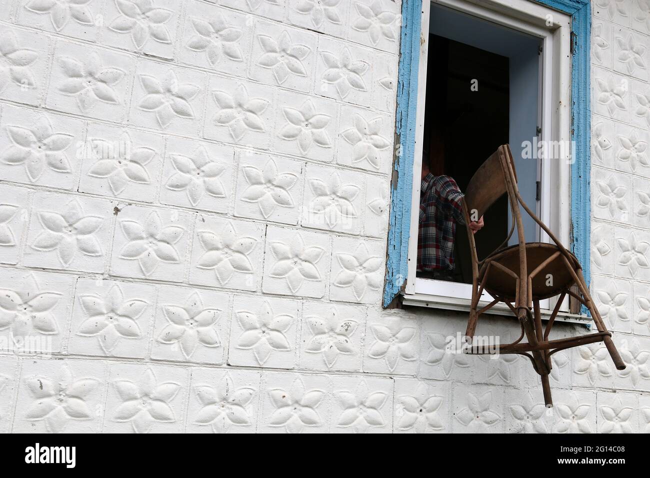 Un uomo getta una vecchia sedia fuori dalla finestra. Tradizione gettare una vecchia cose/ Foto Stock