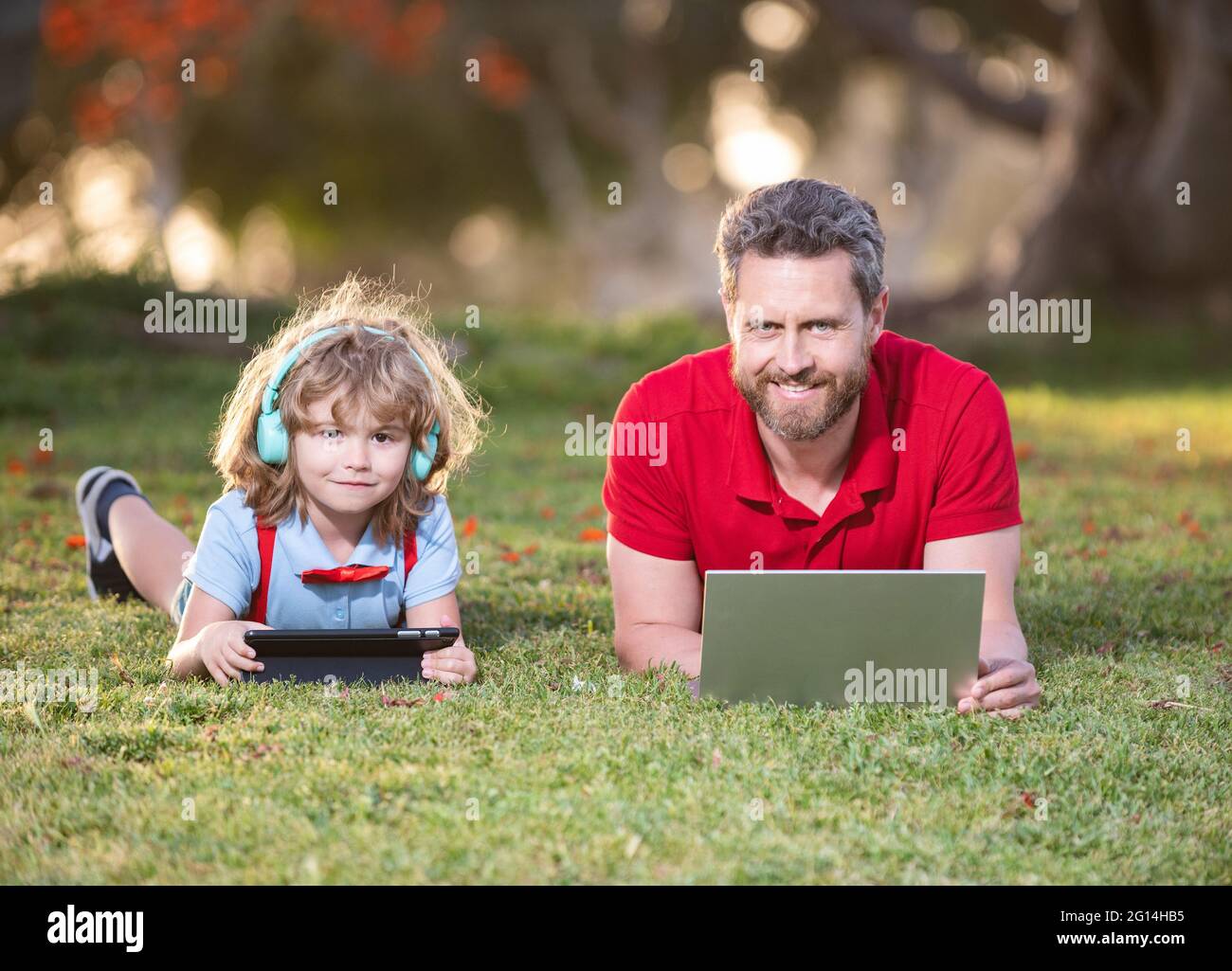 papà e figlio usano il computer portatile per videochiamare o per lezioni  ascoltare musica in cuffia nel parco, in famiglia Foto stock - Alamy