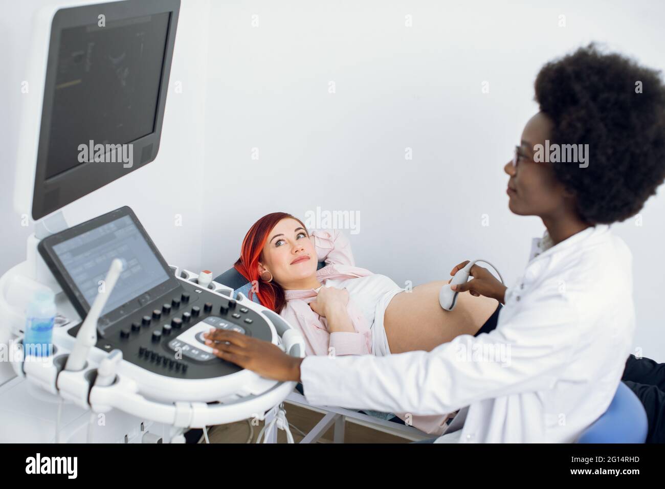 Giovane donna piuttosto incinta che ottiene ecografia dal medico. Professionista sicuro donna africana medico ostetrista, controllare gemelli nella pancia con trasduttore a ultrasuoni scanner Foto Stock