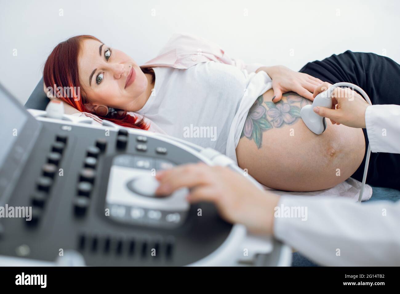 Primo piano immagine ritagliata della dottoressa ostetrica, premendo i pulsanti su un pannello di controllo che esegue la procedura di ecografia per la donna incinta. Focus su bella donna incinta Foto Stock