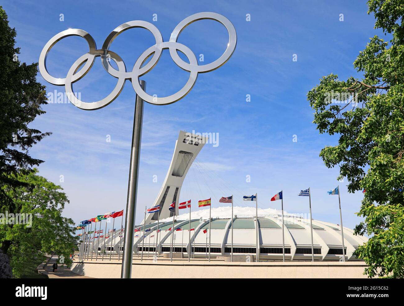 Stadio olimpico di Montreal e torre inclinata in Quebec, tra cui bandiere ondulate multicolore e monumento agli anelli olimpici in primo piano, Canada Foto Stock