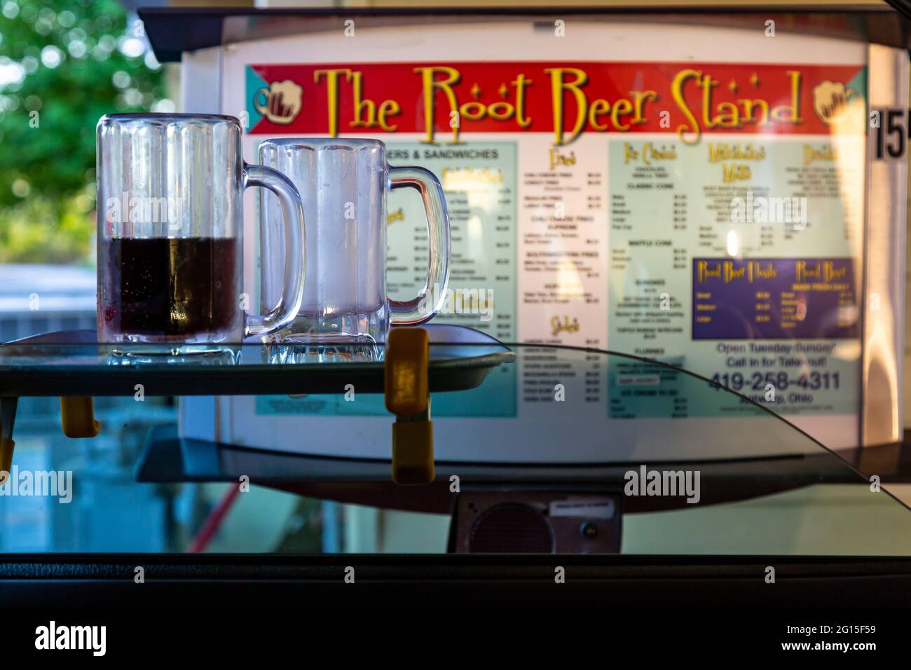 Un menu board drive-in si trova oltre due tazze, una mezza piena, seduto su un vassoio sulla finestra di un veicolo presso il Root Beer Stand ad Anversa, Ohio, Stati Uniti. Foto Stock