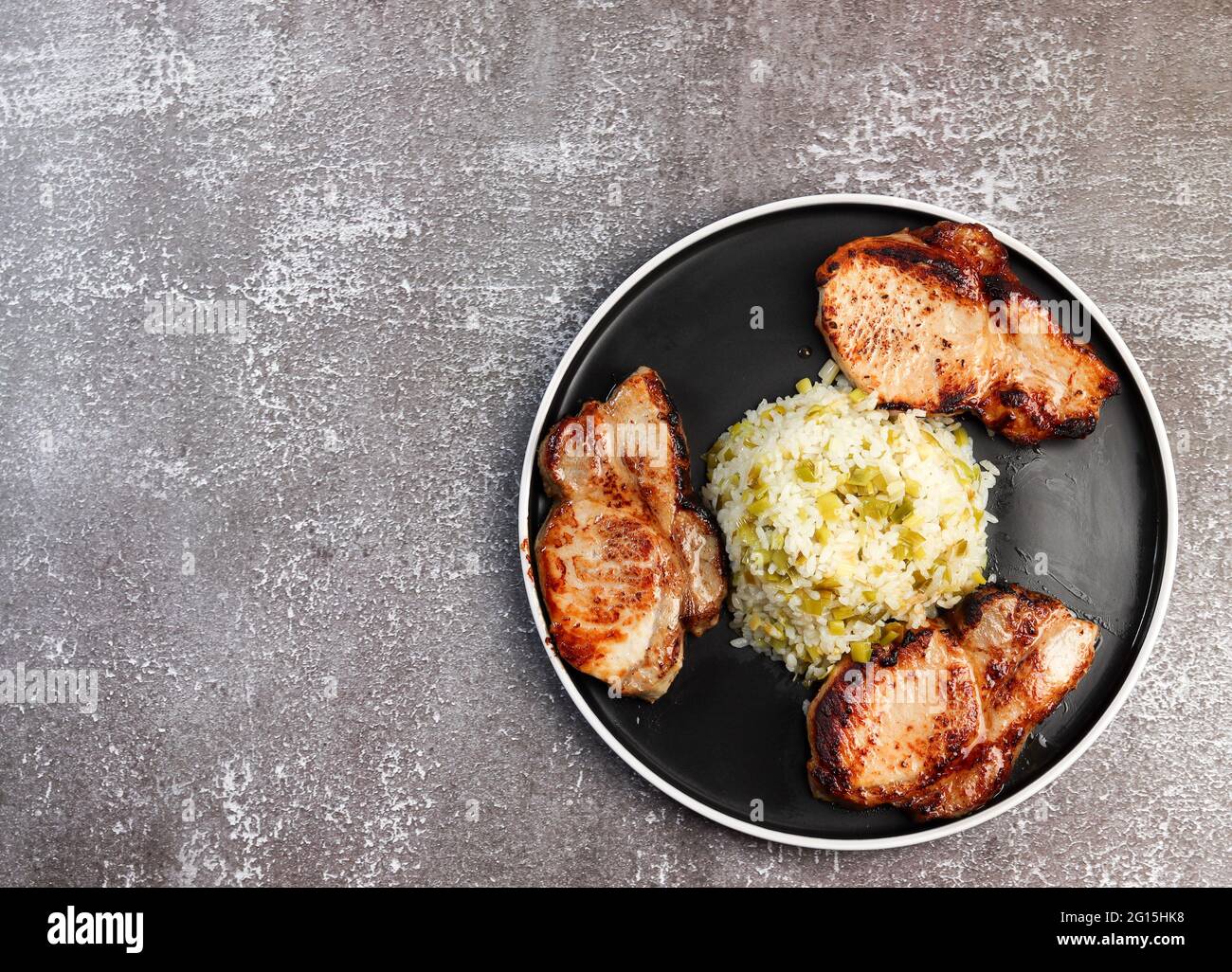 Lombo di maiale con riso su un piatto rotondo su fondo scuro. Vista dall'alto, disposizione piatta Foto Stock