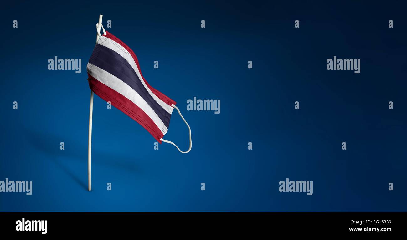 Bandiera sventolante della Thailandia dipinta su maschera medica sul palo. Concetto del banner della lotta contro l'epidemia coronavirus COVID-19. Spazio di copia Foto Stock