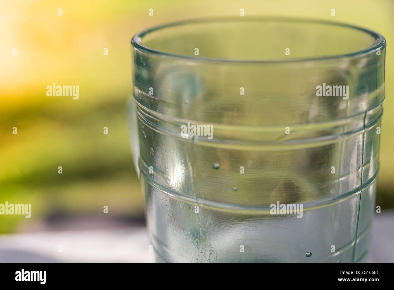 Vetro sfaccettato da vetro verde su sfondo verde naturale sfocato. Tazza di birra, bicchiere d'acqua pulito Foto Stock