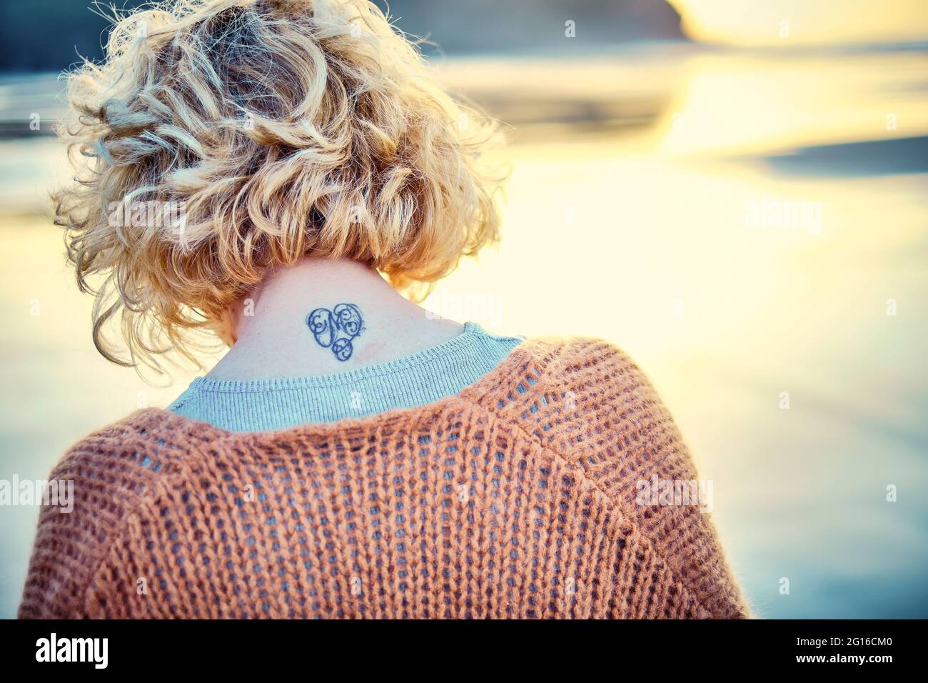 Vista posteriore di una giovane bionda donna caucasica con un tatuaggio in è nuca all'aperto in una spiaggia. Foto Stock