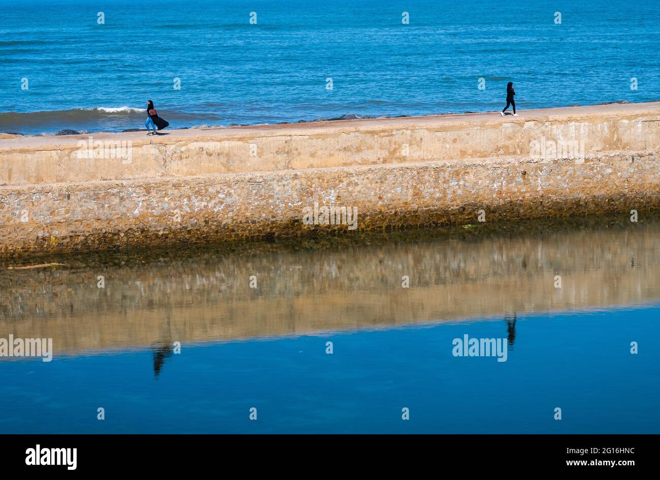 Due donne formano un'immagine speculare mentre camminano vicino al mare nella città marocchina di El Jadida Foto Stock