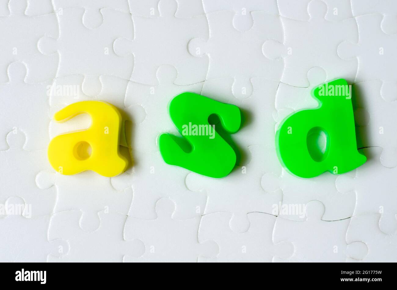 Lettere colorate ASD su uno sfondo di puzzle bianchi. Concetto di giorno di consapevolezza autismo mondiale Foto Stock