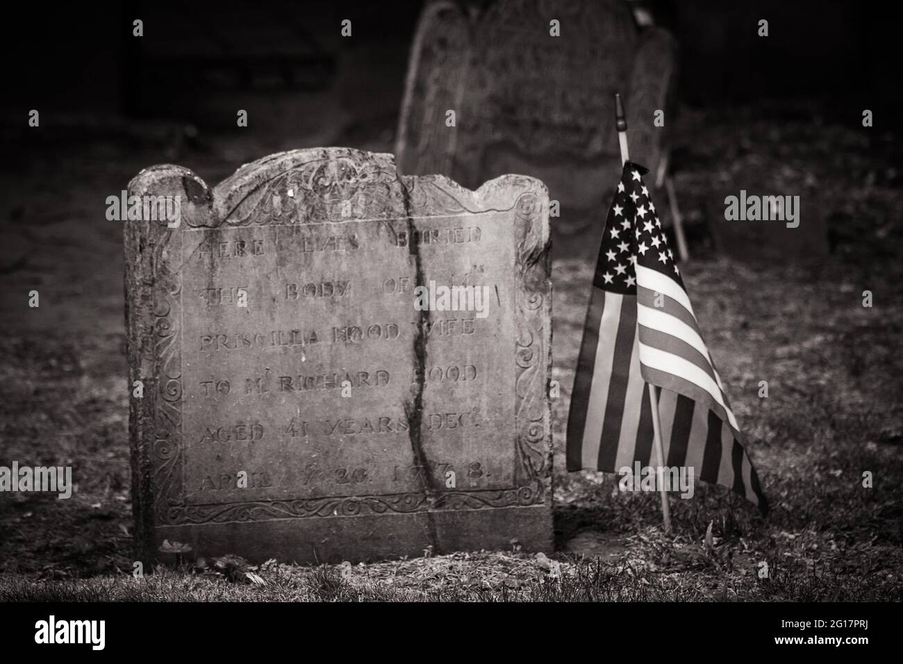 Primo piano di un'antica pietra tomba con una bandiera americana accanto ad essa al Granary Burying Ground a Boston Foto Stock