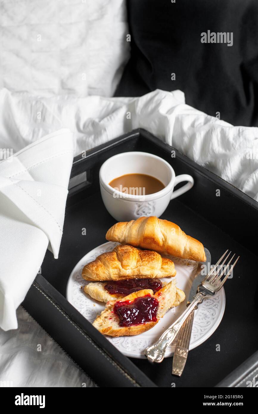Prima colazione a letto: Donne sdraiate a letto con una tazza di caffè,  vassoio con croissant e vasetto di marmellata Foto stock - Alamy