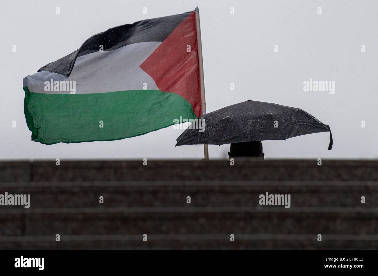 05 giugno 2021, Hessen, Francoforte sul meno: In una pioggia simile al cloudburst, i partecipanti a una manifestazione pro-Palestina con il motto 'Naksa Day, Long Live the Resistance' si sono recati a Francoforte. Solo la bandiera e l'ombrello di un partecipante possono essere visti. Foto: Boris Roessler/dpa Foto Stock