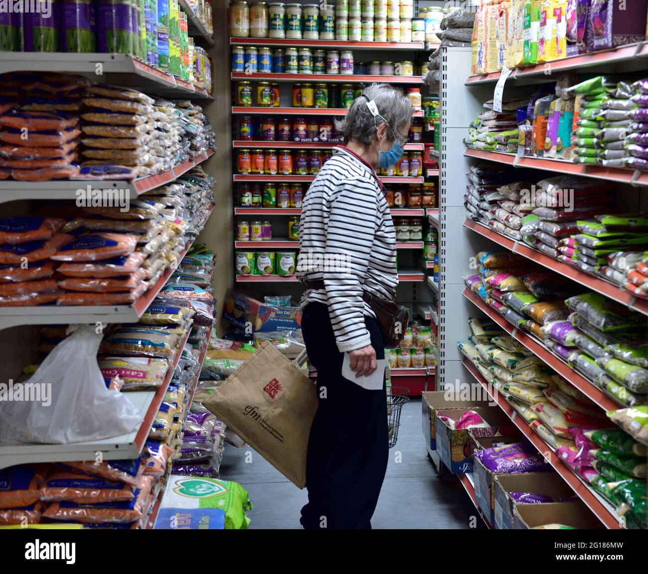 Shopping cercando sacchetti di fagioli secchi e lenticchie in un piccolo negozio di alimentari d'angolo locale ben rifornito, Regno Unito Foto Stock