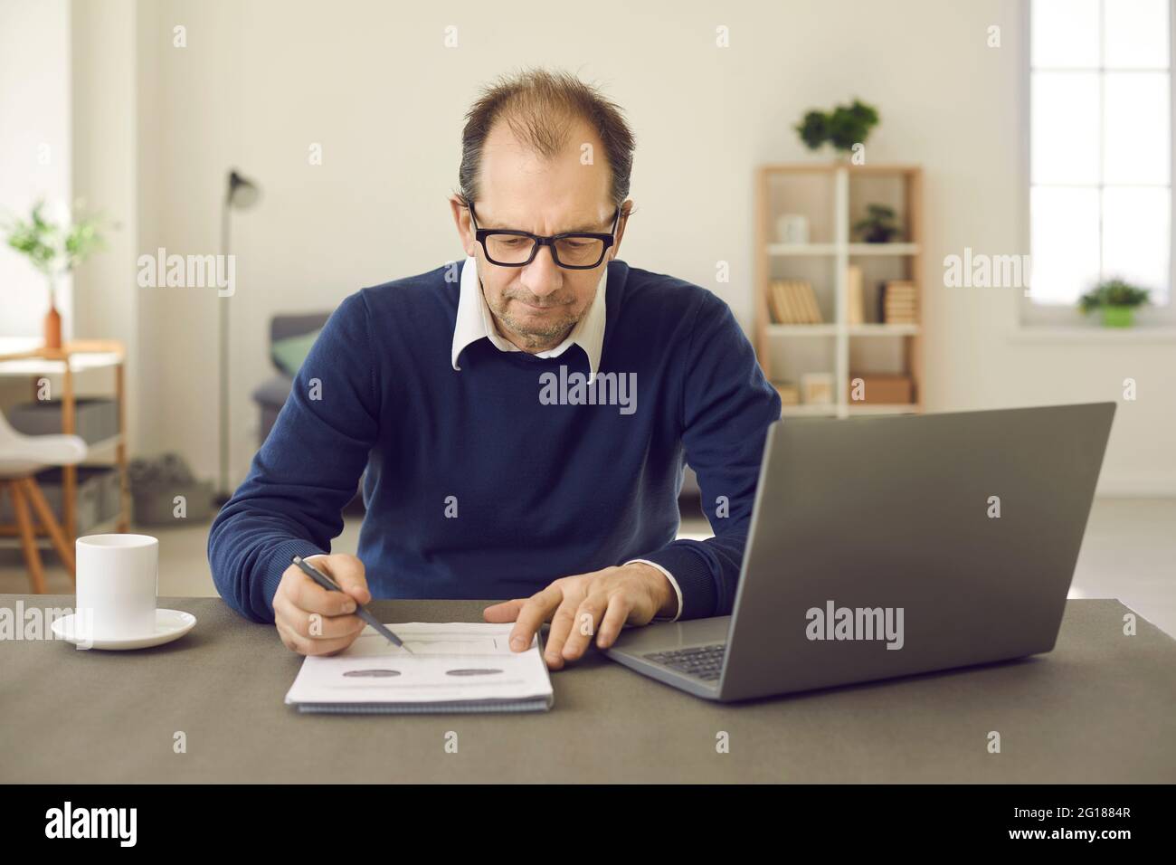 L'uomo d'affari prepara i dati per il rapporto di vendita confrontando i grafici su carta e su laptop. Foto Stock