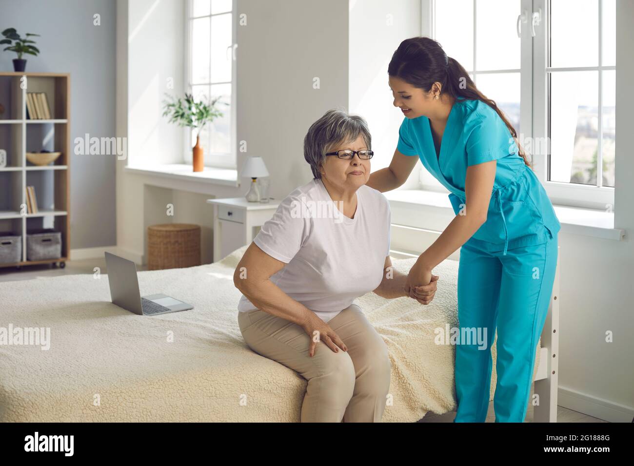 Un'infermiera sorridente che sostiene la paziente che assiste la donna anziana si alzano dal letto Foto Stock