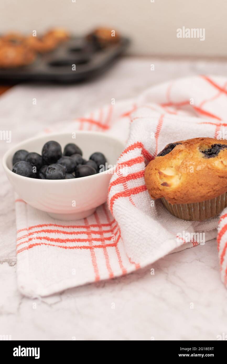 Muffin al mirtillo su un asciugamano rosso fiancheggiato da una ciotola di mirtilli. Foto Stock